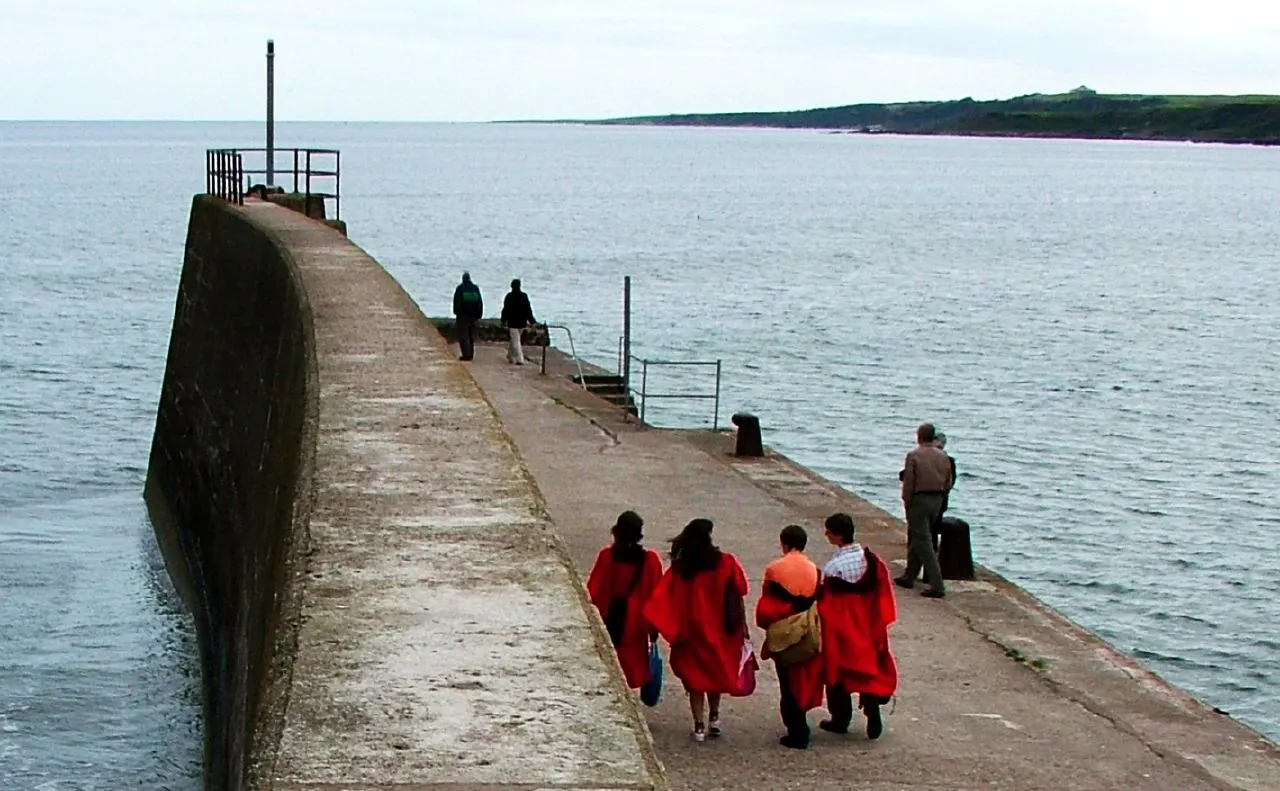 Students at the University of St Andrews in their red gowns, walking along the town's pier.